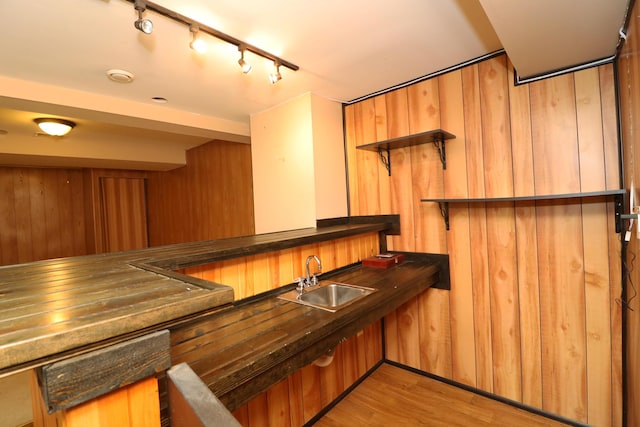 bar with rail lighting, wood walls, sink, and light hardwood / wood-style flooring