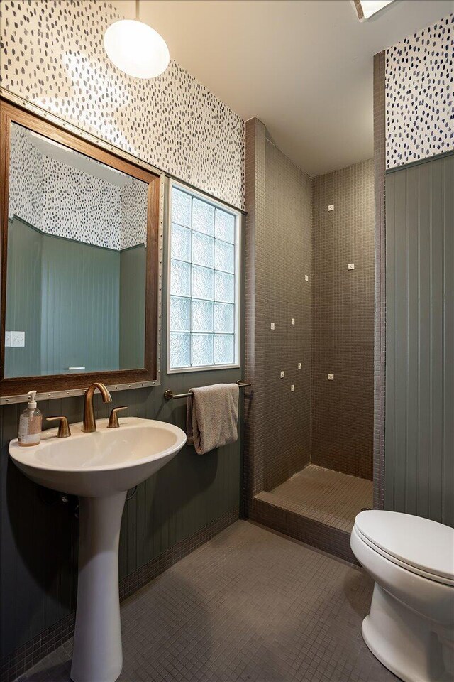 bathroom with tile patterned flooring, a tile shower, and toilet