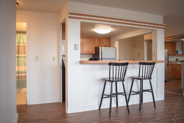 kitchen featuring kitchen peninsula, stainless steel fridge, dark hardwood / wood-style floors, and a kitchen breakfast bar