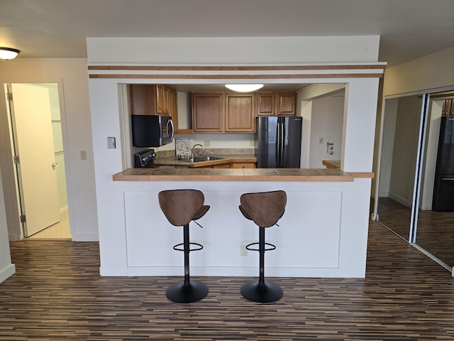 kitchen with sink, dark hardwood / wood-style flooring, kitchen peninsula, a breakfast bar, and black appliances