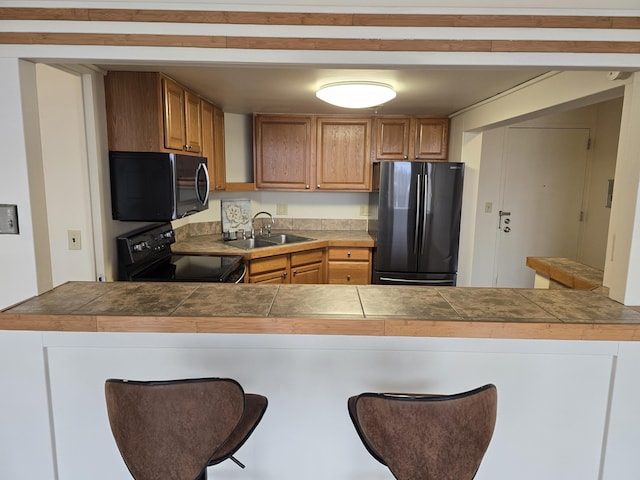 kitchen with a breakfast bar, tile countertops, kitchen peninsula, and black appliances