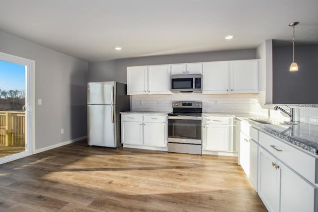 kitchen featuring pendant lighting, sink, light hardwood / wood-style flooring, appliances with stainless steel finishes, and white cabinetry