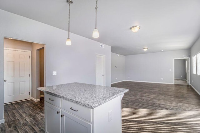 kitchen with decorative light fixtures, a kitchen island, light stone counters, and dark wood-type flooring