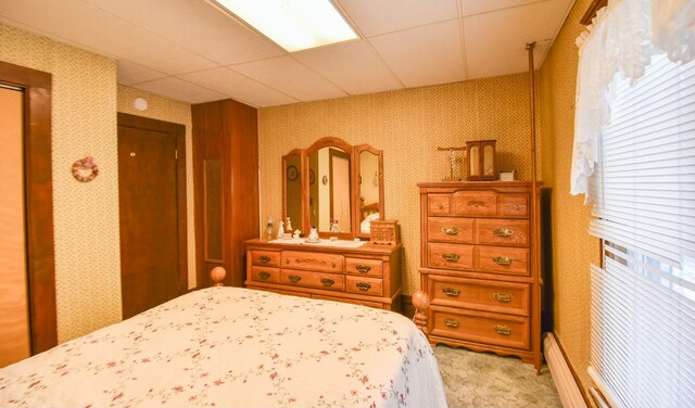 carpeted bedroom with a paneled ceiling and a baseboard radiator