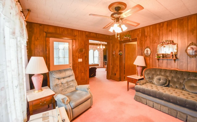 living room with ceiling fan with notable chandelier, light colored carpet, and wood walls