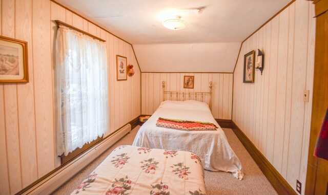 bedroom featuring wood walls, carpet, vaulted ceiling, and a baseboard heating unit