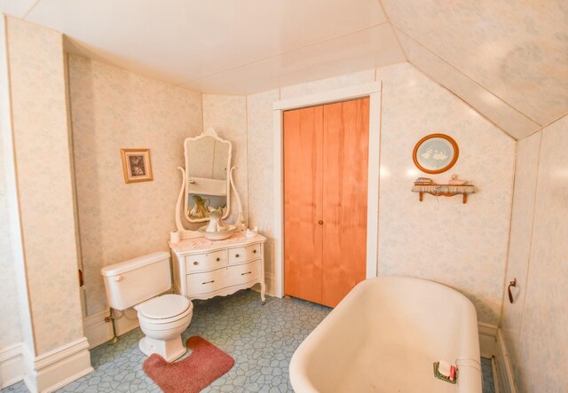 bathroom with a bathtub, toilet, and lofted ceiling