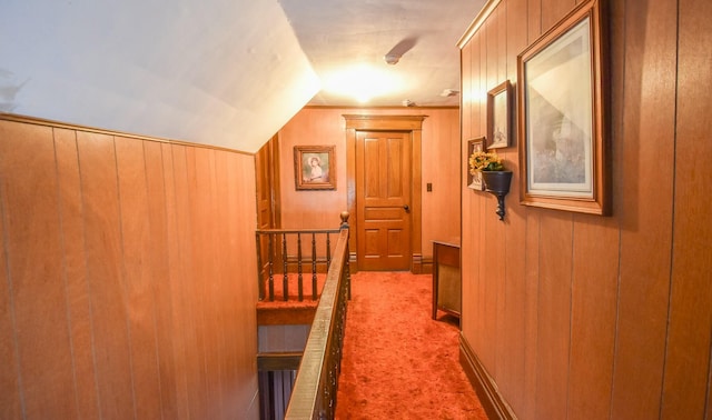 hallway featuring carpet flooring, wooden walls, and lofted ceiling