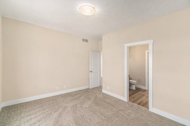 unfurnished bedroom with connected bathroom, a textured ceiling, and carpet