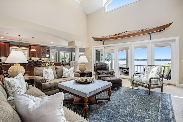 living room featuring a water view, crown molding, carpet floors, decorative columns, and a high ceiling