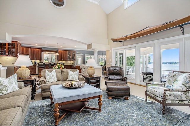 living room featuring a water view, crown molding, carpet floors, decorative columns, and a high ceiling