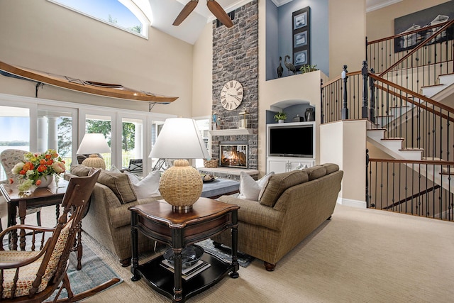 carpeted living room with a stone fireplace, ceiling fan, and a towering ceiling