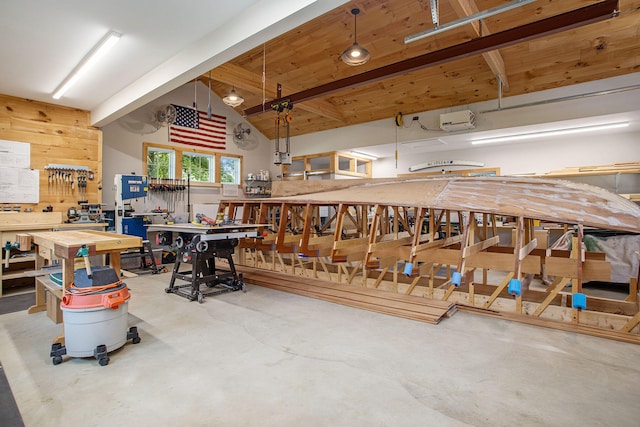 misc room featuring vaulted ceiling with beams, wooden walls, a workshop area, and concrete floors