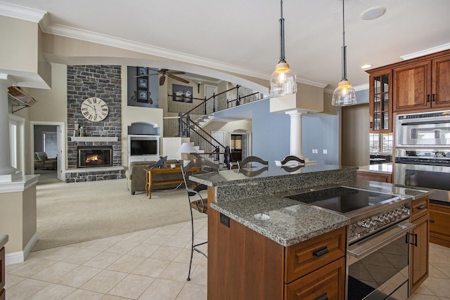 kitchen with ornate columns, stainless steel stove, a fireplace, a kitchen bar, and dark stone counters