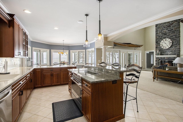 kitchen featuring light tile patterned flooring, a stone fireplace, a breakfast bar area, decorative light fixtures, and stainless steel appliances