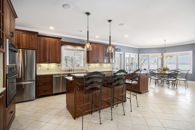 kitchen featuring light stone counters, appliances with stainless steel finishes, a kitchen breakfast bar, a kitchen island, and pendant lighting