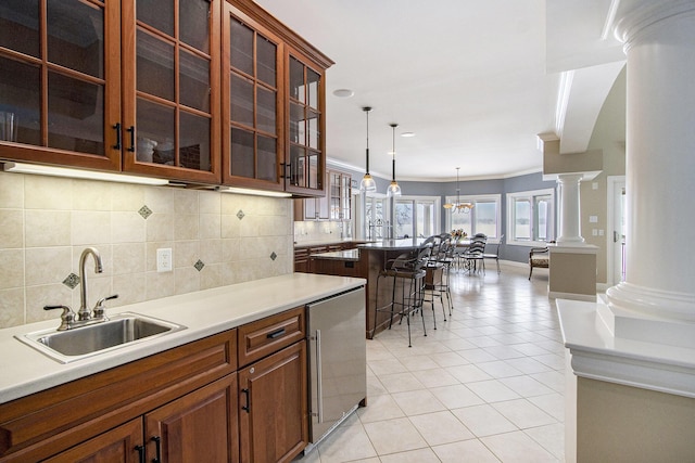 kitchen with sink, a breakfast bar area, decorative light fixtures, light tile patterned floors, and decorative columns