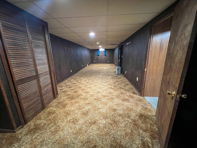 basement with a paneled ceiling, wood walls, and carpet floors