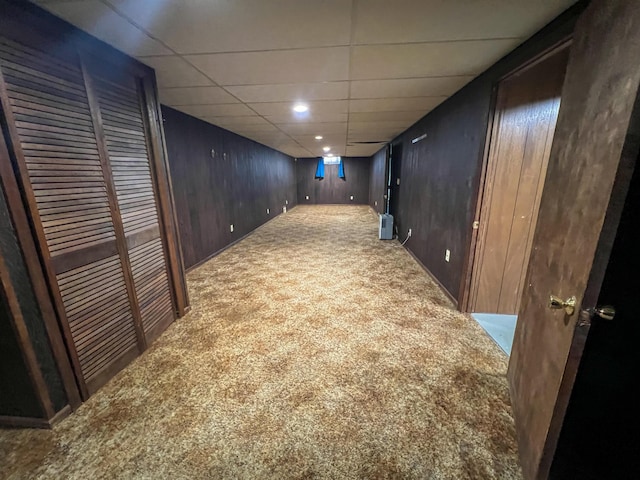 basement featuring wooden walls, a drop ceiling, and carpet