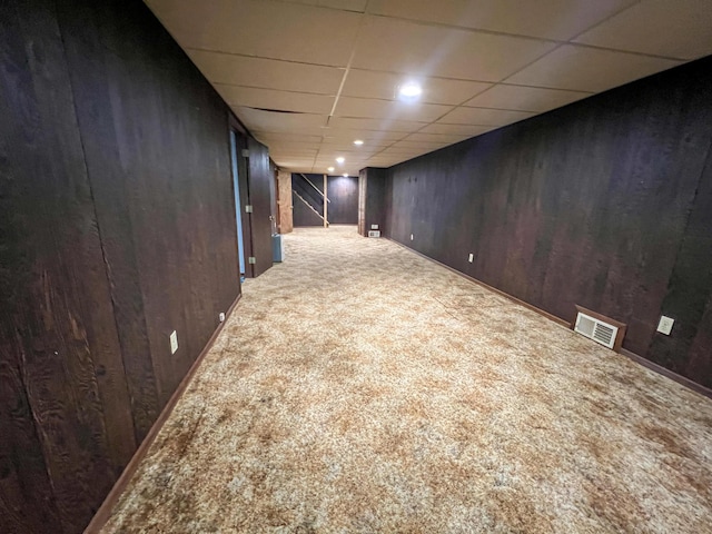 basement featuring carpet flooring, a paneled ceiling, and wooden walls