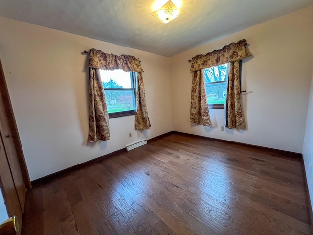 spare room featuring dark wood-type flooring and a baseboard heating unit