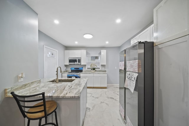 kitchen with sink, appliances with stainless steel finishes, white cabinetry, light stone counters, and kitchen peninsula