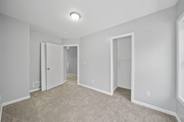 unfurnished bedroom with a walk in closet, light colored carpet, and a closet