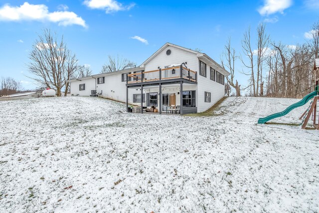 snow covered property with a playground, a balcony, and central air condition unit