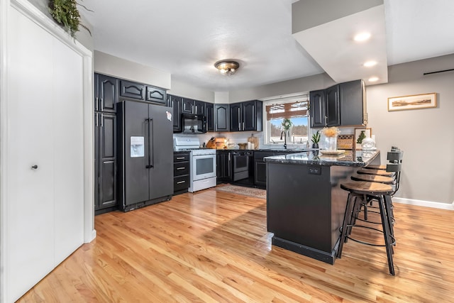 kitchen featuring high end refrigerator, white range oven, dark stone countertops, light hardwood / wood-style floors, and a breakfast bar area