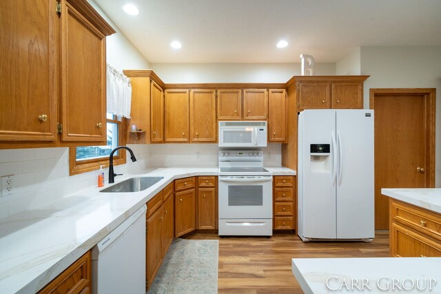 kitchen featuring white appliances, sink, decorative backsplash, light hardwood / wood-style floors, and light stone counters