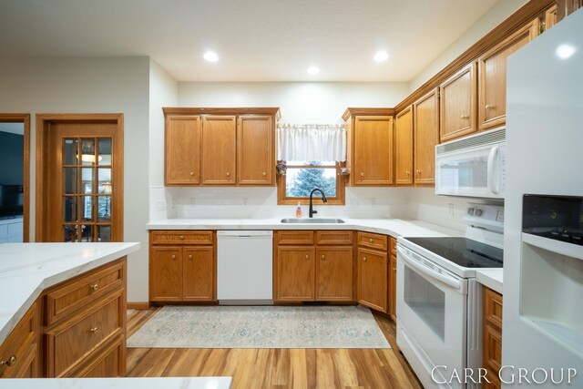 kitchen with sink, light stone counters, light hardwood / wood-style floors, white appliances, and decorative backsplash