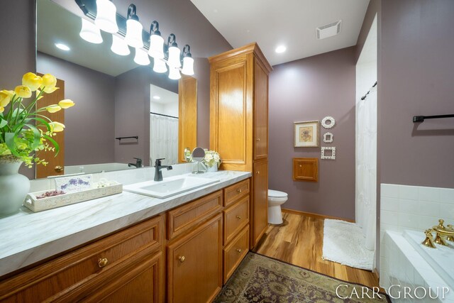 bathroom with hardwood / wood-style flooring, vanity, toilet, and tiled tub