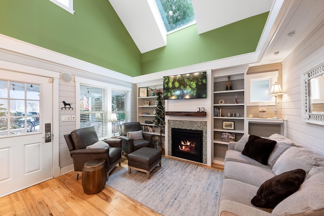 living room featuring a skylight, high vaulted ceiling, wooden walls, a fireplace, and light wood-type flooring