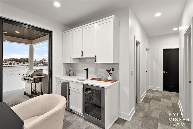 bar with white cabinets, decorative backsplash, wine cooler, and sink