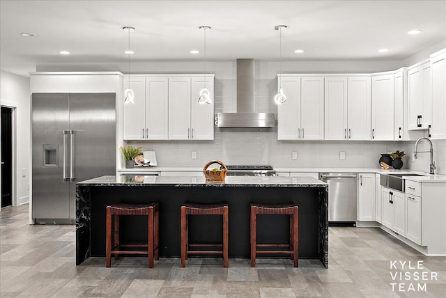 kitchen with appliances with stainless steel finishes, sink, wall chimney exhaust hood, and a kitchen island