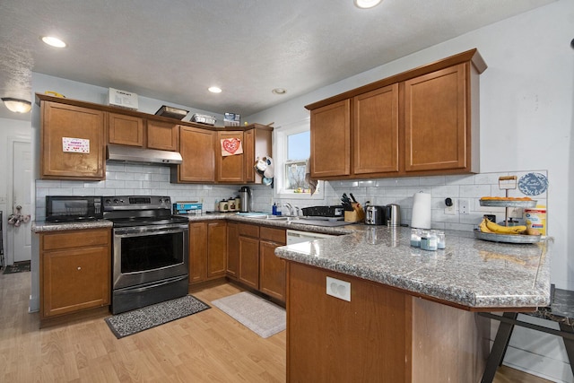 kitchen featuring a kitchen breakfast bar, kitchen peninsula, dark stone counters, stainless steel range with electric cooktop, and light wood-type flooring