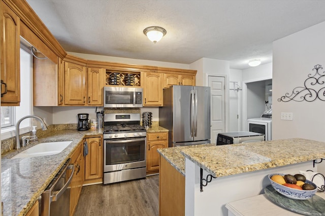 kitchen with light stone countertops, sink, stainless steel appliances, washer / clothes dryer, and a kitchen bar