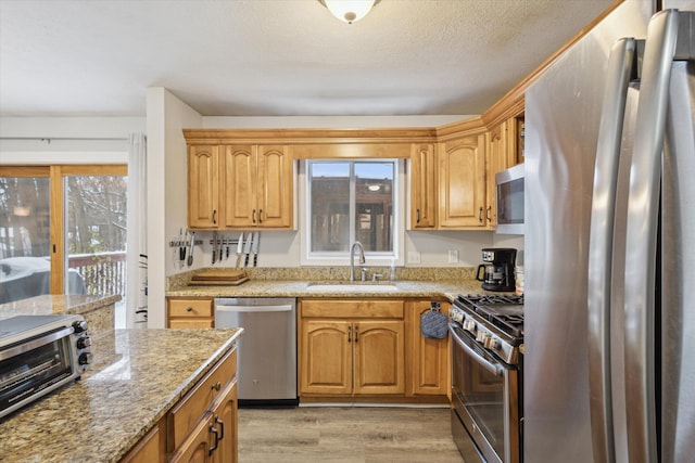 kitchen with appliances with stainless steel finishes, light stone counters, a textured ceiling, sink, and light hardwood / wood-style floors