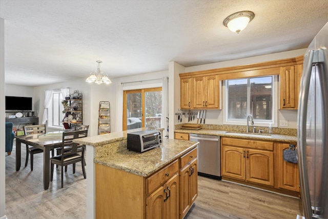 kitchen with pendant lighting, a center island, sink, light hardwood / wood-style flooring, and appliances with stainless steel finishes