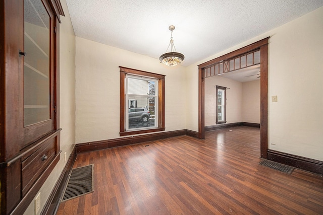 empty room with ceiling fan with notable chandelier, a textured ceiling, and dark hardwood / wood-style flooring