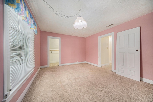 unfurnished bedroom featuring carpet, a textured ceiling, a walk in closet, and a closet