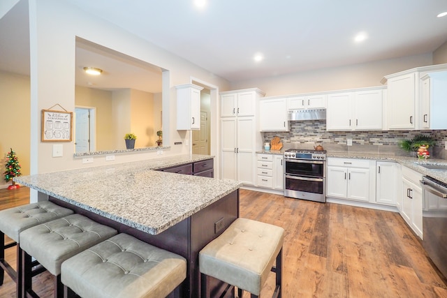 kitchen featuring white cabinetry, light stone countertops, kitchen peninsula, a breakfast bar area, and appliances with stainless steel finishes