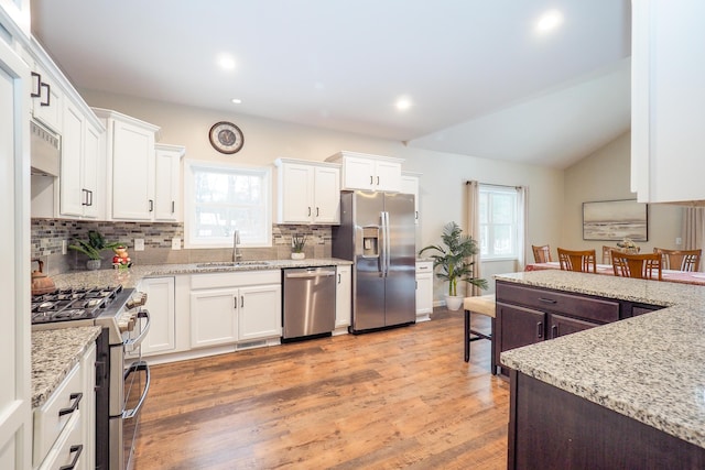 kitchen with appliances with stainless steel finishes, vaulted ceiling, sink, white cabinets, and light hardwood / wood-style floors