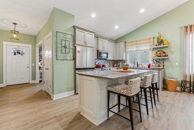 kitchen featuring stainless steel appliances, a kitchen breakfast bar, light hardwood / wood-style floors, decorative light fixtures, and a kitchen island