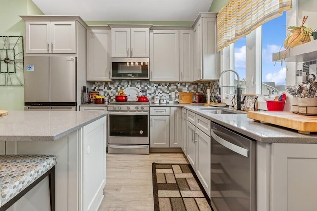 kitchen with light stone countertops, decorative backsplash, light wood-type flooring, stainless steel appliances, and sink