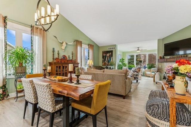 dining room featuring ceiling fan with notable chandelier, light hardwood / wood-style floors, plenty of natural light, and lofted ceiling