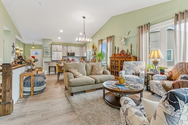 living room with light hardwood / wood-style floors, vaulted ceiling, a wealth of natural light, and a chandelier