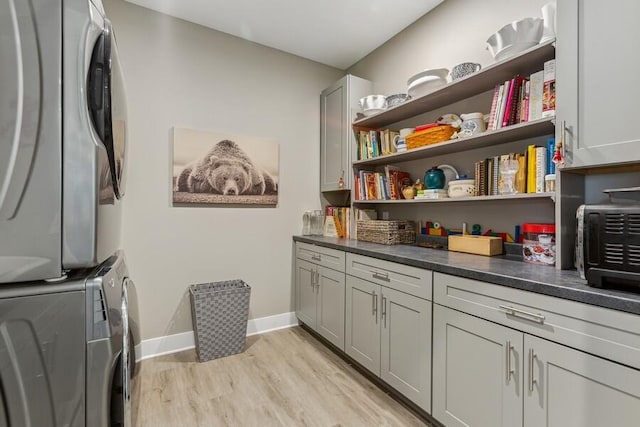 clothes washing area with cabinets, stacked washing maching and dryer, and light hardwood / wood-style floors