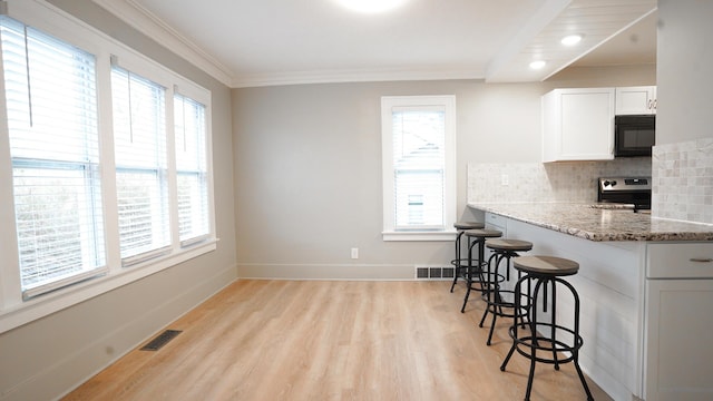 kitchen with a breakfast bar, stainless steel range with electric stovetop, white cabinets, light stone countertops, and backsplash