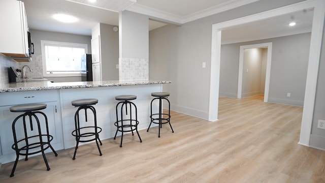 kitchen with kitchen peninsula, light stone counters, white cabinetry, and backsplash